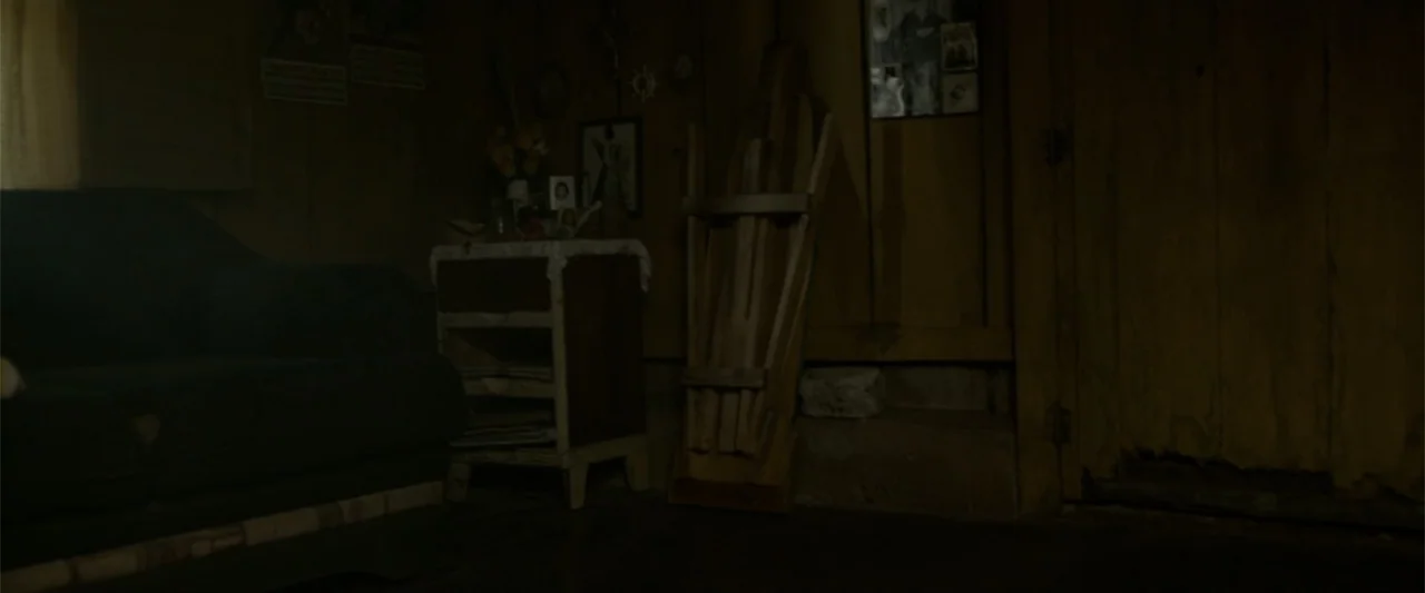 I Dream in Another Language (2017) movie still: wide — A dimly lit room features wooden walls, a worn sofa, and miscellaneous household items. The…