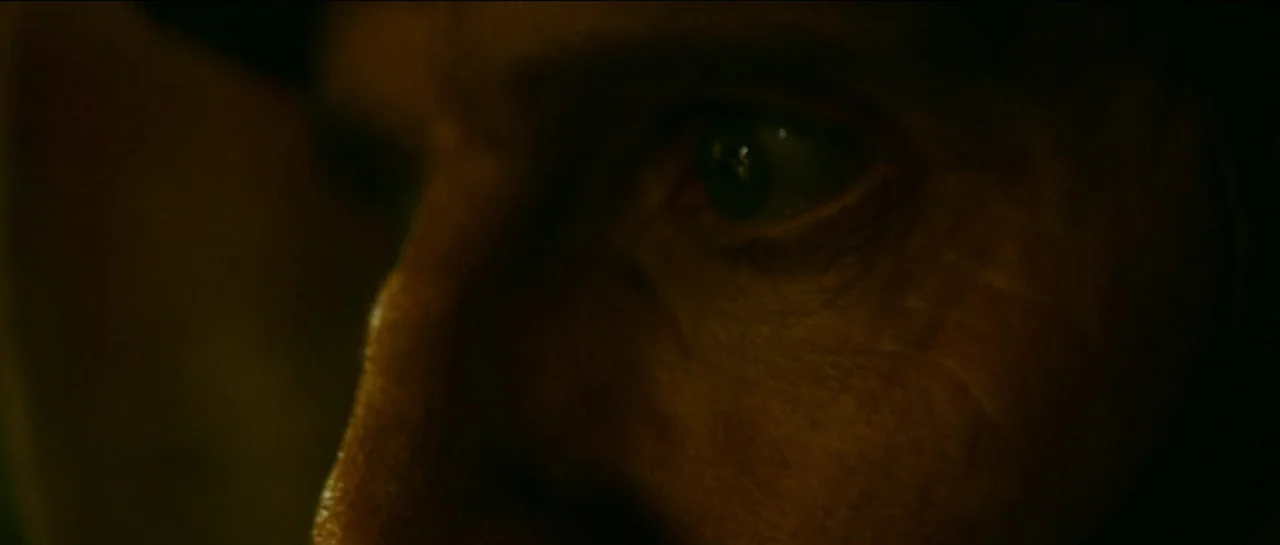 The Killer (2023) movie still: closeup — A dark, underexposed environment leaves only a portion of a human face visible. The skin texture and eye…