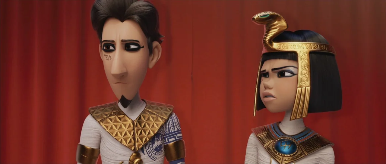 Mummies (2023) movie still: medium — An interior space features two animated characters standing in front of a red curtain. A man and a woman in…