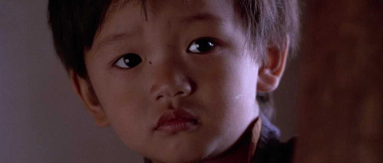 Kundun (1997) movie still: closeup — A close-up shot focuses on the face of a young East Asian child. The background is out of focus and nondescript.