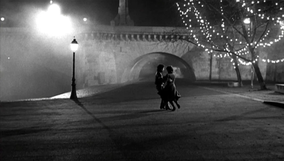 The Tango Lesson (1997) movie still: wide — A stone bridge spans a foggy nocturnal waterfront area illuminated by string lights. A couple dances…
