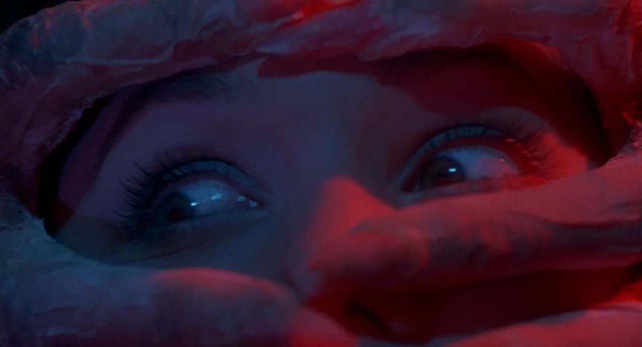 Inferno (1980) movie still: closeup — A close-up reveals a person's eyes framed by an object obscuring the lower face. The scene is illuminated by…