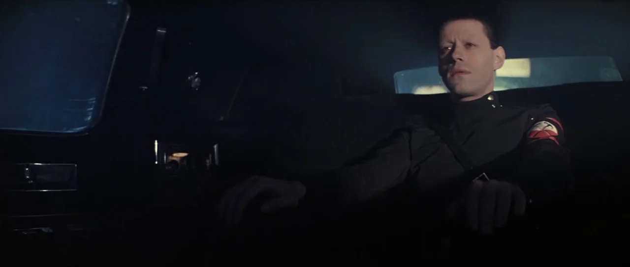 Pink Floyd The Wall (1982) movie still: medium — The interior of a dark car is mostly obscured by deep shadows at night. A man in a dark military…