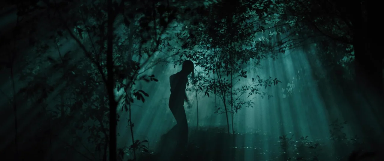 No One Will Save You (2023) movie still: wide — A dark, dense forest filled with thick fog and prominent vertical light beams. A lone woman in…
