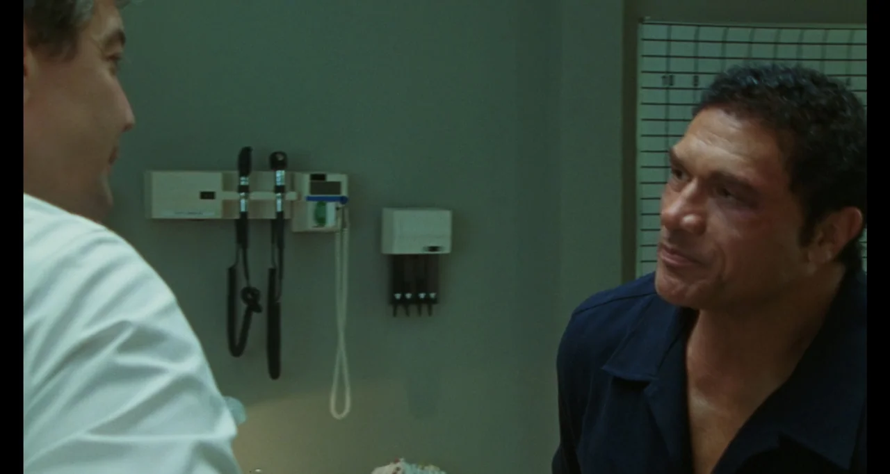 The Smashing Machine (2025) movie still: medium — A clinical medical examination room features pale green walls and medical equipment mounted…