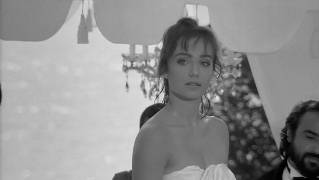 Under The Cherry Moon (1986) movie still: medium — An outdoor gathering under a white fabric canopy with hanging crystal chandeliers. A woman stands…