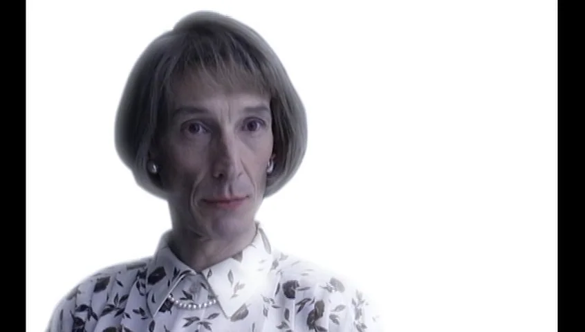 The Tracey Fragments (2007) movie still: closeup — A studio setting with a completely white background behind the subject. An elderly woman stands…
