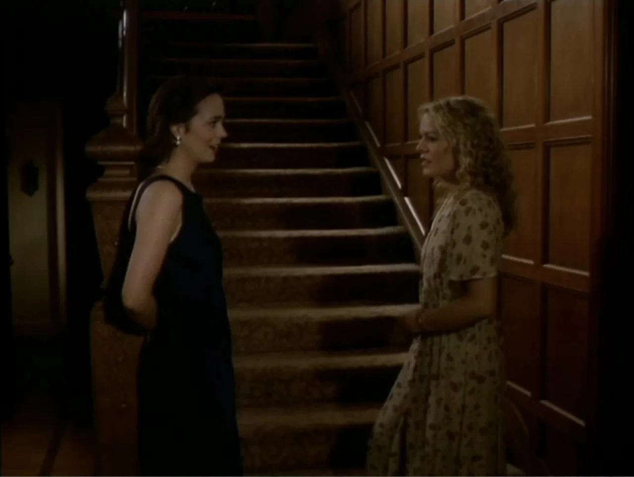 At the Midnight Hour (1995) movie still: medium — A wooden staircase landing features dark wood paneling and a carpeted floor. Two women in formal…
