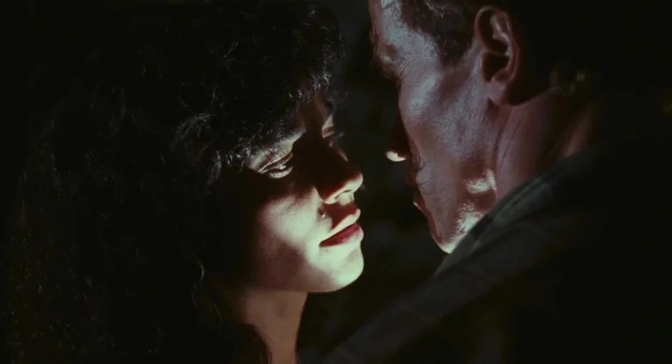 Total Recall (1990) movie still: closeup — A dark, dimly lit environment obscures the background details. A man and woman stand closely facing each…