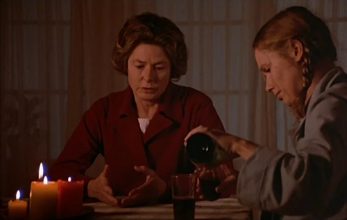 Autumn Sonata (1978) movie still: medium — Two women sit at a dimly lit wooden table covered by a simple tablecloth. One woman pours dark wine into…