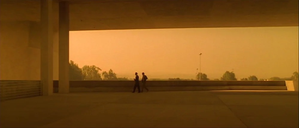 Gattaca (1997) movie still: wide — A wide concrete terrace features massive pillars and an expansive, hazy orange desert view. Two men in suits walk…