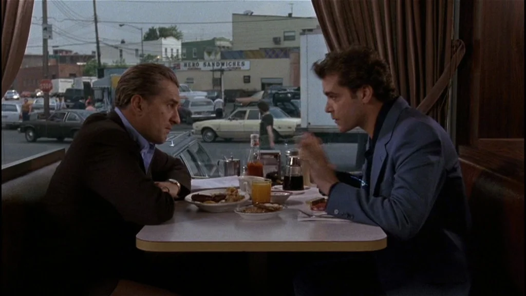 Goodfellas (1990) movie still: medium — A booth in a diner looks out through a large window toward a parking lot. Two men sit at the table with…