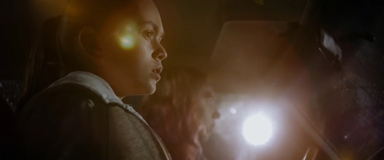 The Monster (2016) movie still: closeup — The interior of a vehicle is illuminated at night by a strong oncoming light. A young girl in the…