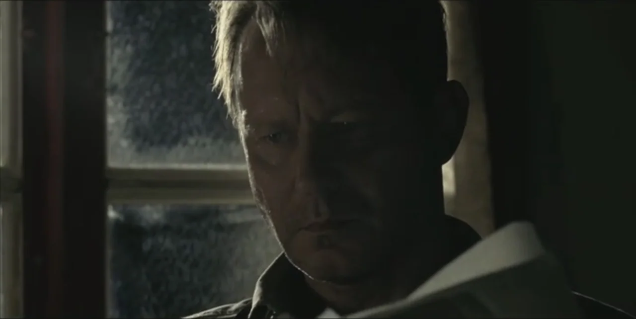 Exorcist: The Beginning (2004) movie still: closeup — A dark interior room features a window with frosted glass letting in dim light. A man holds a…