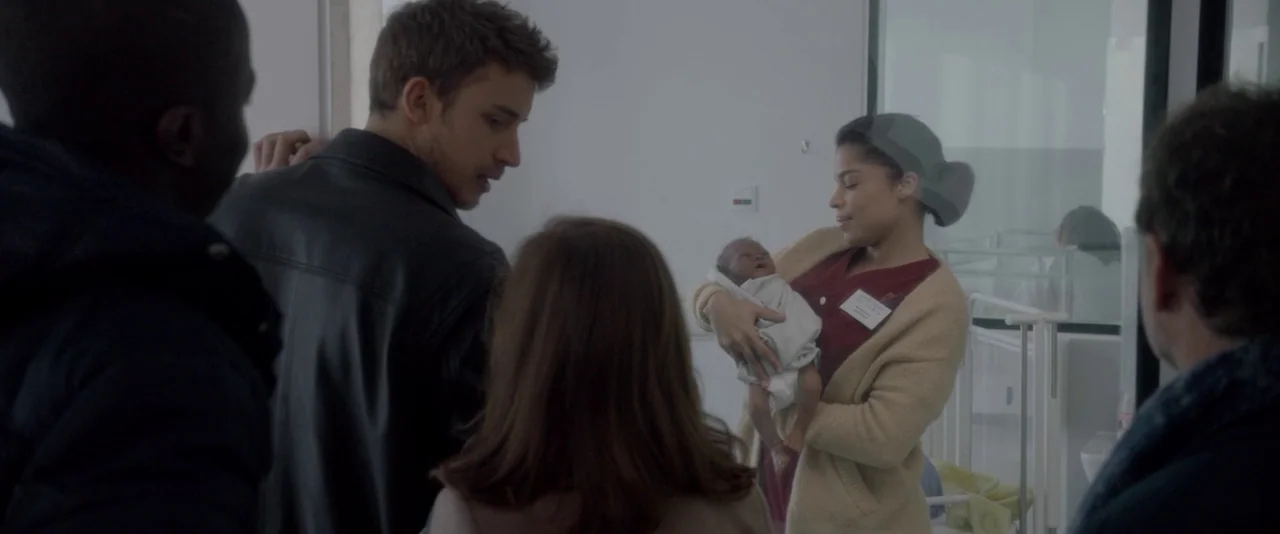 Elle (2016) movie still: medium — A sterile hospital ward features white walls and a large glass window divider. A nurse wearing scrubs and a…