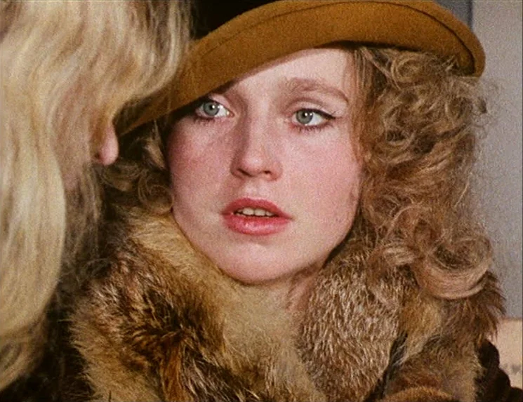 Rio Das Mortes (1971) movie still: closeup — A close-up shot of a young woman wearing a felt hat and fur collar. A second person is partially…