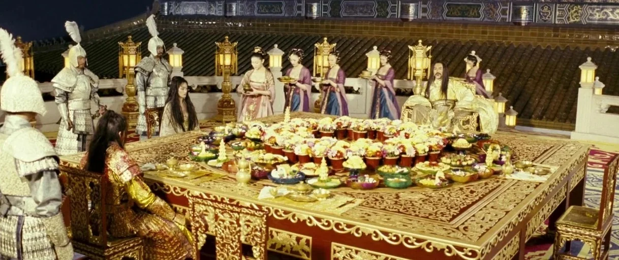 Curse of the Golden Flower (2006) movie still: wide — An imperial banquet takes place on a wide terrace overlooking a dark night sky. Many figures…