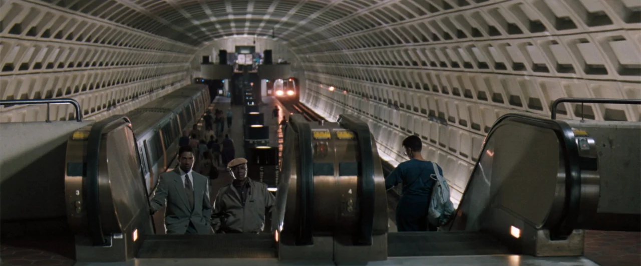 The Pelican Brief (1993) movie still: wide — A subterranean subway platform features vaulted concrete ceilings and parallel escalator banks. Several…