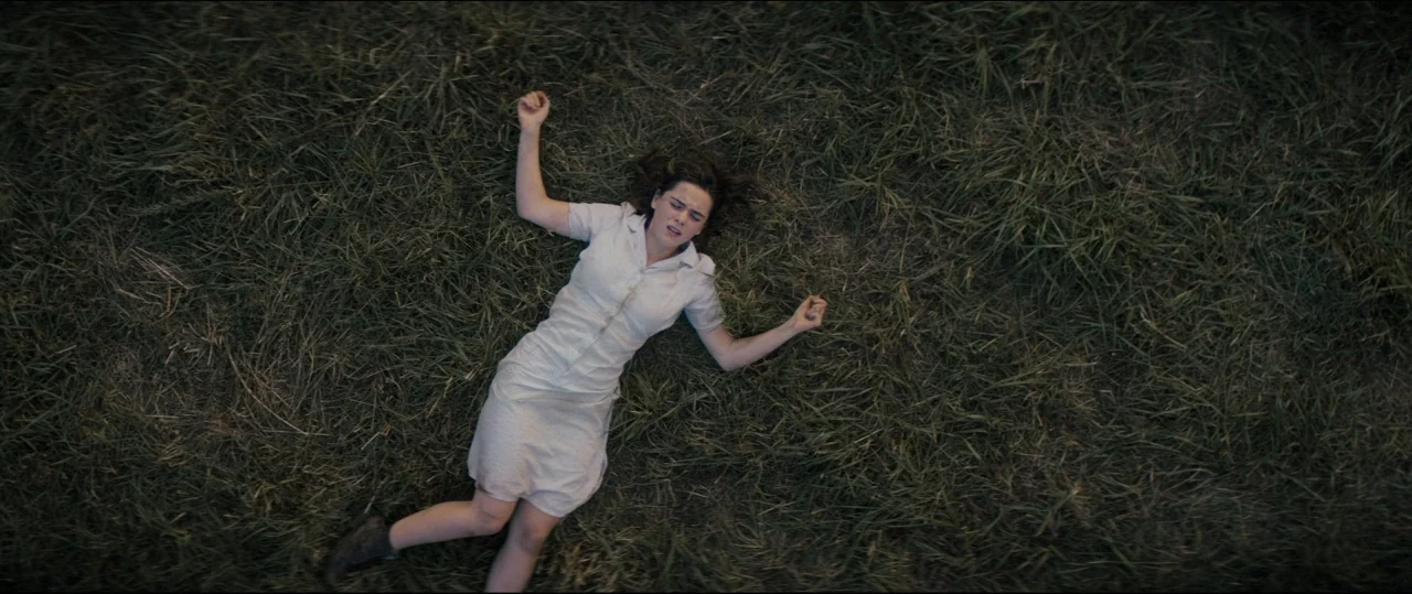 One & Two (2015) movie still: fullbody — A person lies supine in a field of tall, wild grass. The woman wears a cream dress and rests with her arms…
