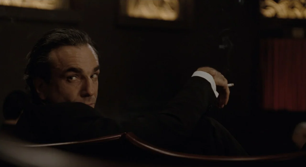The Great Beauty (2013) movie still: medium — A dimly lit room with dark paneling features decorative gold-accented wall molding in the background.…
