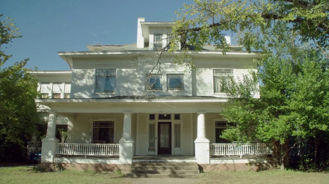 Everybody Wants Some!! (2016) movie still: wide — A two-story, white-sided house with a large front porch sits behind mature green trees. The…
