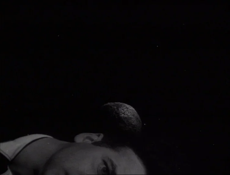 Eraserhead (1977) movie still: closeup — A night landscape features a dark sky with a prominent moon. A man lies on the ground looking upward.