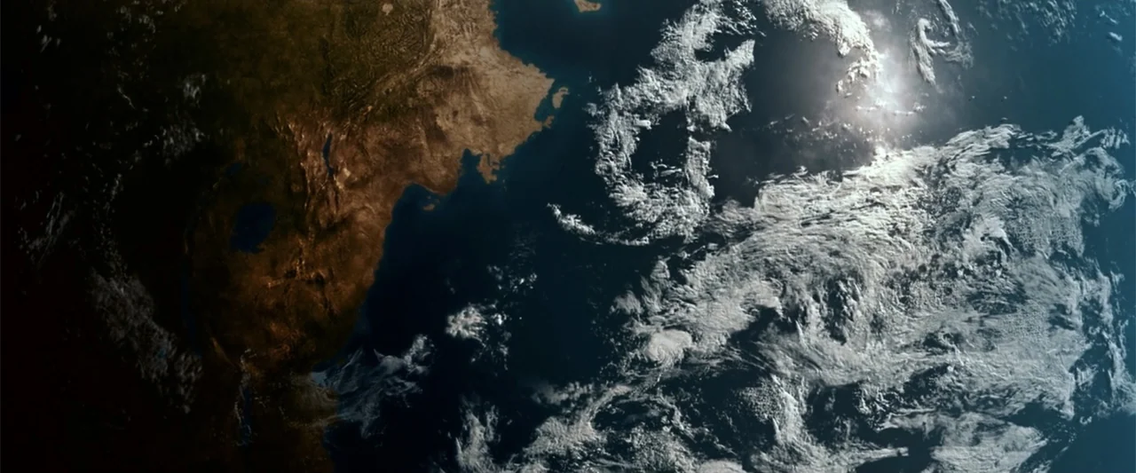 2012 (2009) movie still: establishing — A view of the earth from orbit showing parts of the continent and ocean. Thick white clouds swirl over dark…