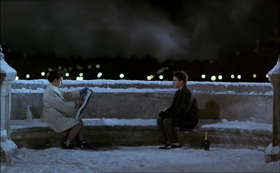 Les Amants Du Pont Neuf (The Lovers on the Bridge) (1991) movie still: wide — A snowy stone terrace overlooks a dark city at night with distant…
