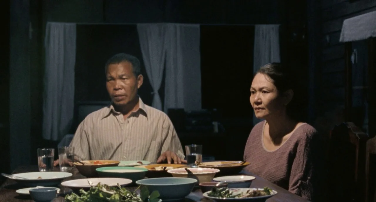 Uncle Boonme Who Can Recall His Past Lives (2010) movie still: medium — A dimly lit room at night with a table set for dinner. A man and a woman sit…