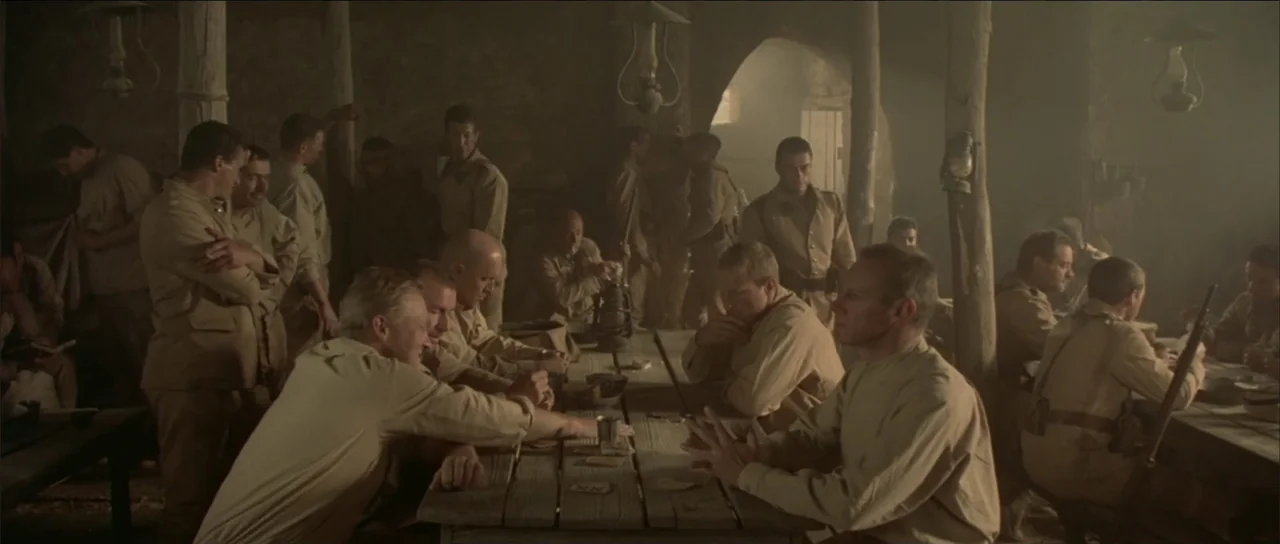 Legionario (2025) movie still: wide — A smoky, dimly lit mess hall features rough timber pillars and wooden tables. Soldiers in khaki uniforms sit…