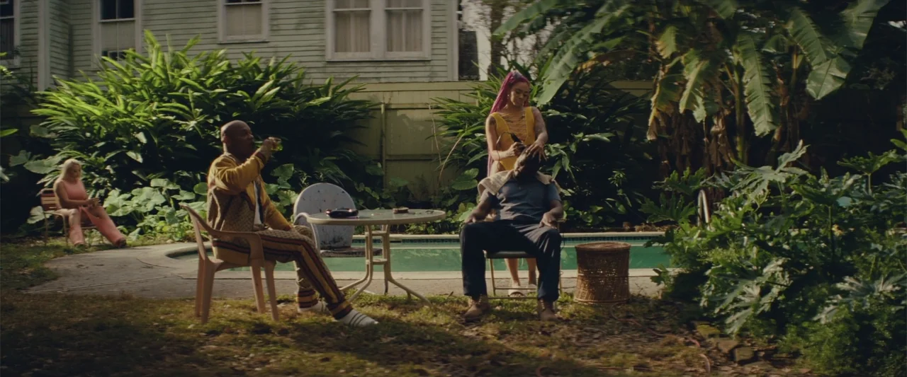Queen & Slim (2019) movie still: wide — A residential backyard features a swimming pool surrounded by overgrown tropical plants and trees. A woman…