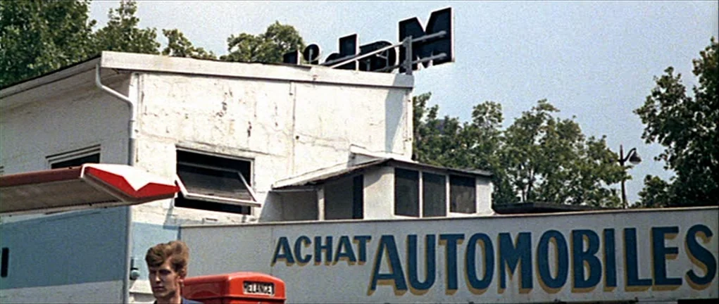 Two or Three Things I Know About Her (2 ou 3 choses que je sais d’elle) (1967) movie still: medium — A white painted commercial building features a…