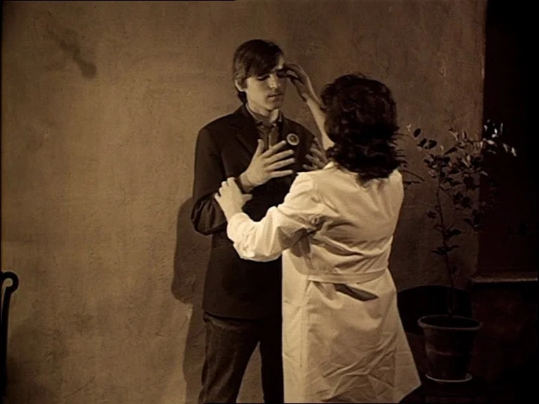 Mirror (Зеркало, Zerkalo) (1975) movie still: fullbody — A plain interior room with a textured beige wall and a potted plant. A woman wearing a…