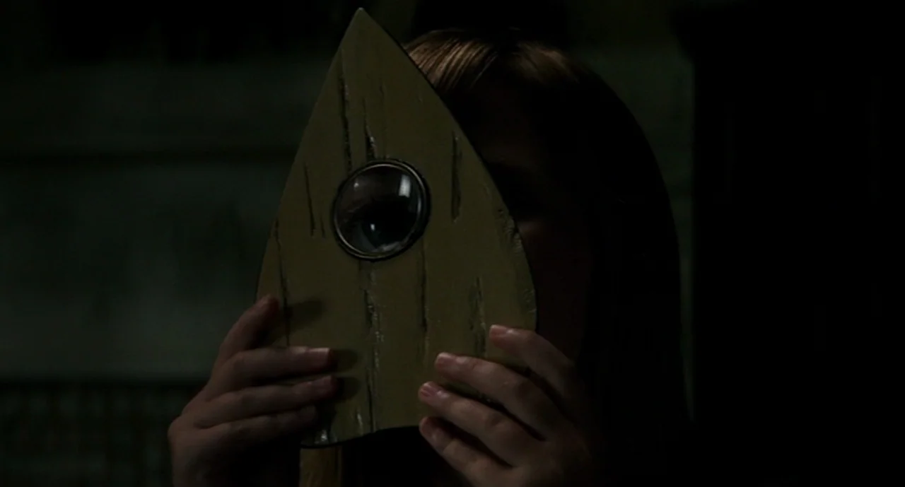 Ouija: Origin of Evil (2016) movie still: closeup — A dimly lit room interior features a person holding a wooden ouija board pointer. The person…
