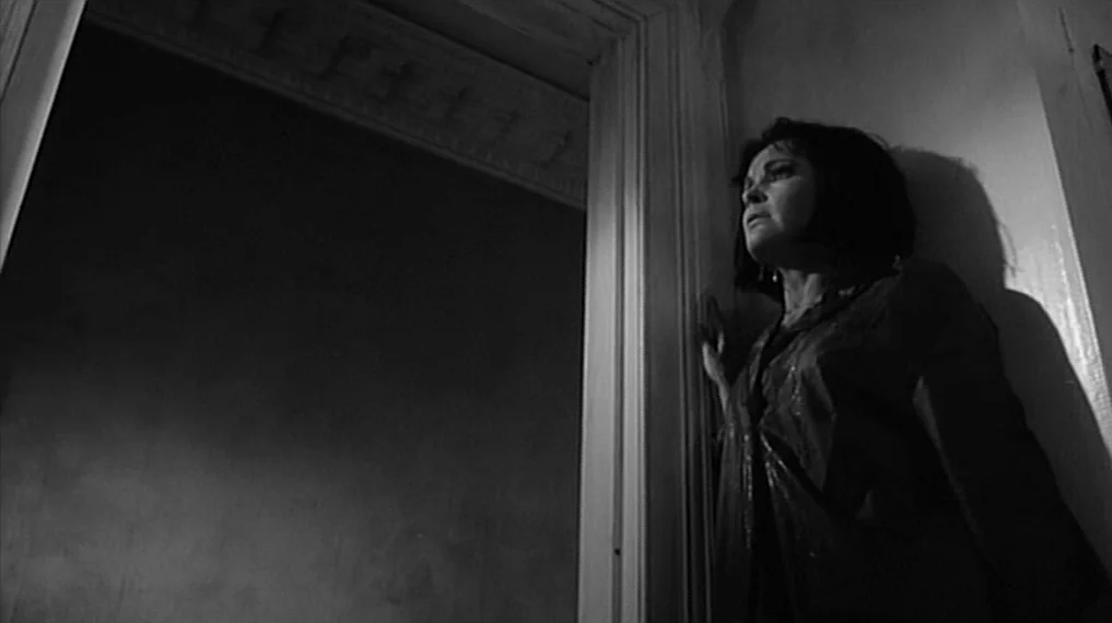 Repulsion (1965) movie still: medium — A dark, narrow doorway transitions into an illuminated room with simple molding. A woman stands in the…