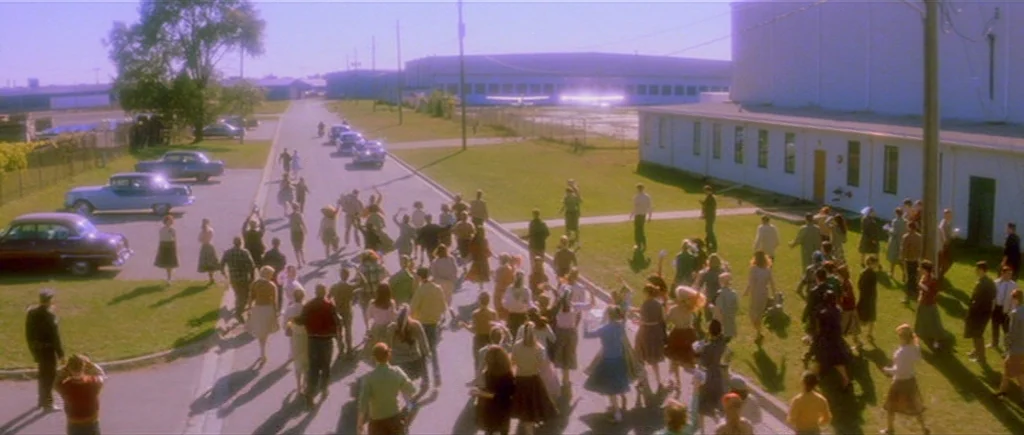 Where The Truth Lies (2005) movie still: wide — A large crowd moves away from an industrial facility toward the camera on a road. Numerous people in…