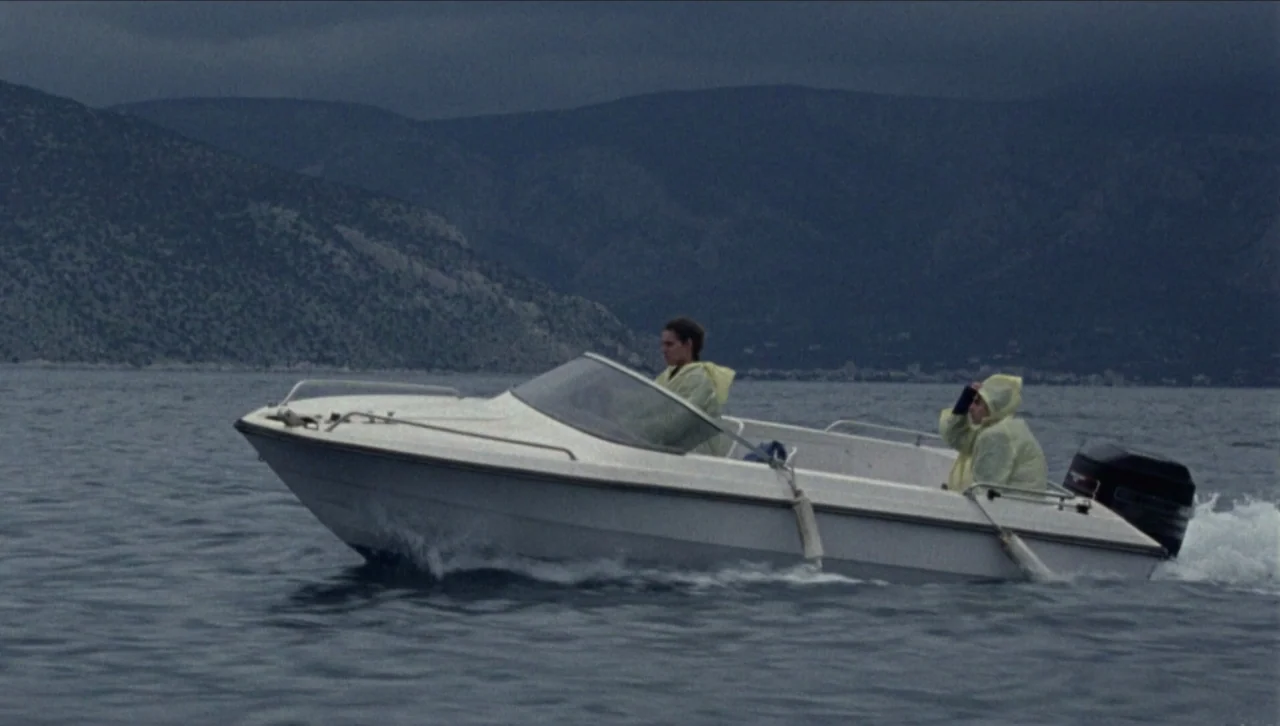 Attenberg (2010) movie still: wide — A small white motorboat moves across a grey, choppy body of water under overcast skies. Two people wearing…