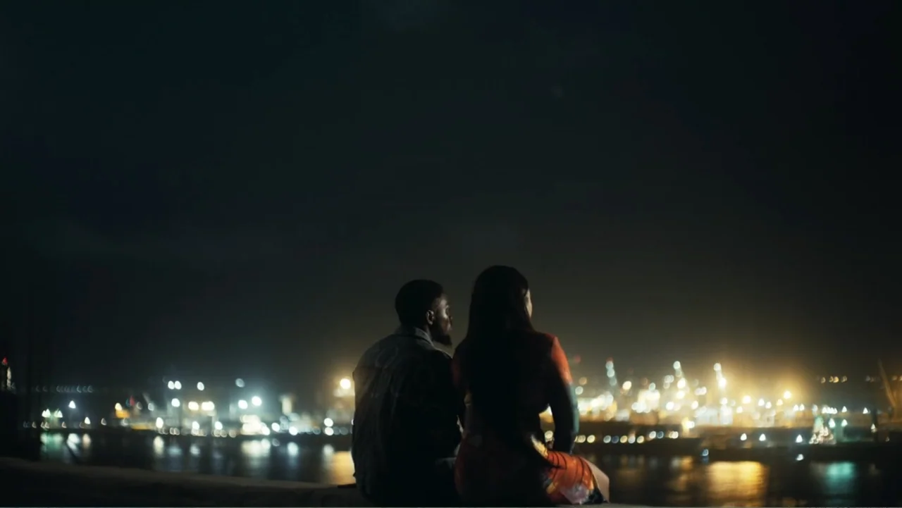Gangs of Lagos (2023) movie still: medium — A dark concrete ledge overlooks a sprawling industrial harbor with distant glowing artificial lights. A…