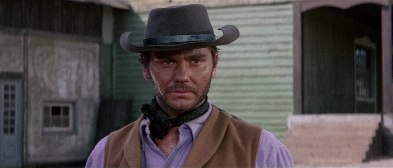 Texas, Adios (1966) movie still: medium — A wooden town building with a covered porch stands in the background. A man wearing a cowboy hat and vest…