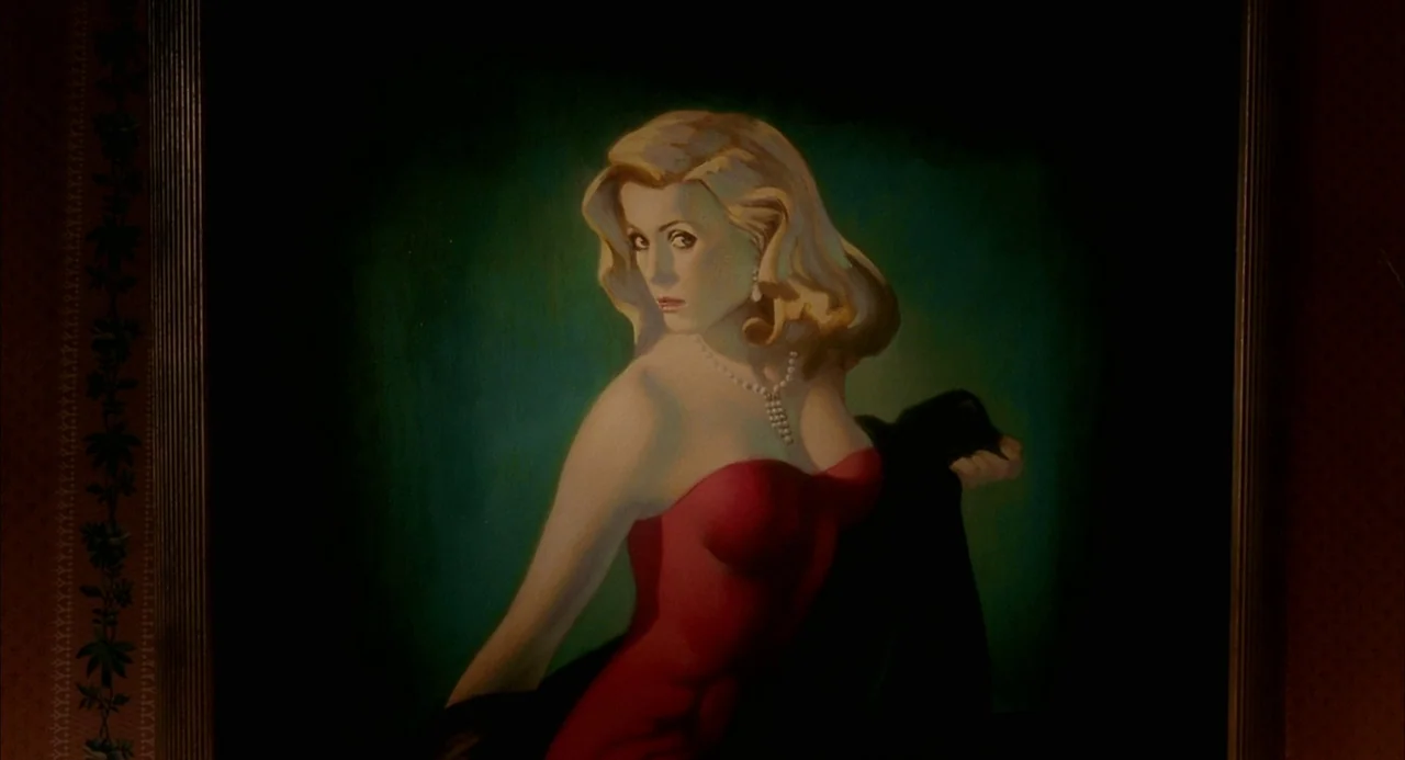 8 Women (2002) movie still: closeup — A framed oil painting depicts a blonde woman wearing a red dress. The woman poses in a three-quarter turn…