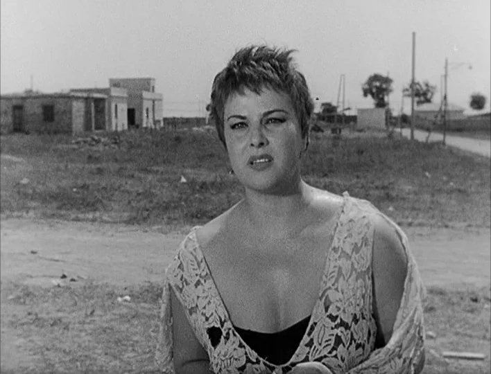 Nights of Cabiria (1957) movie still: medium — A woman stands in a desolate vacant lot near some unfinished residential buildings. She is positioned…