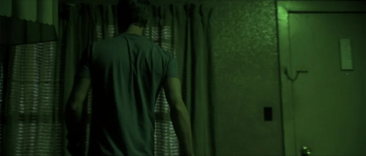 Joy Ride (2001) movie still: medium — A dimly lit room at night with a man standing in front of curtains. The green illumination highlights the…