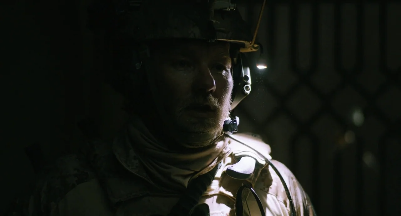 Zero Dark Thirty (2012) movie still: closeup — A dark, enclosed space with a metal grate structure faintly visible in the background. A soldier in…