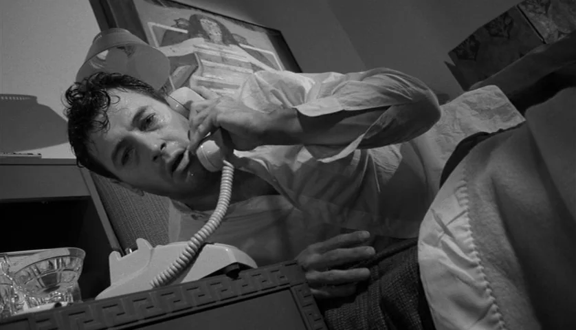 Seconds (1966) movie still: medium — A dark hotel room features a framed painting hanging above a low bed. A man wearing a white shirt lies across…