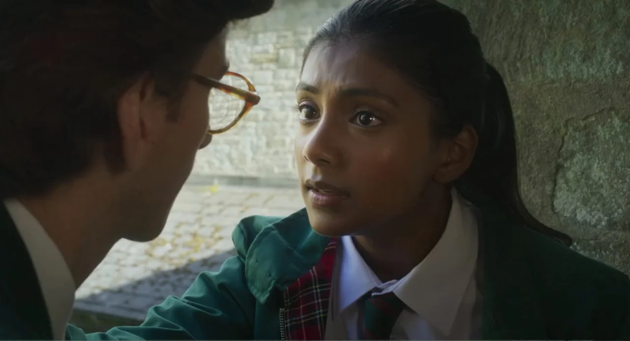 How to Date Billy Walsh (2024) movie still: medium — A stone-walled courtyard provides the backdrop for two students in matching green blazers. The…