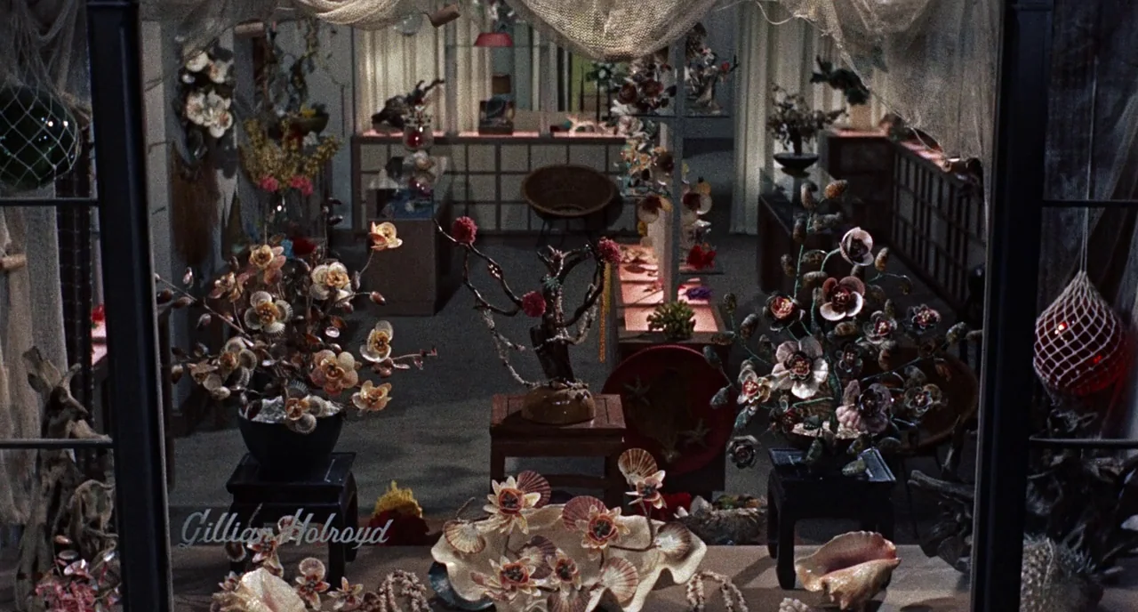 Bell Book and Candle (1958) movie still: establishing — A quiet gift shop features shelves filled with decorative shell art and artifacts. The…