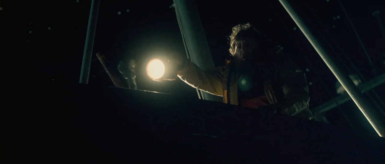Grabbers (2012) movie still: medium — A dark boat deck at night is illuminated only by a harsh handheld flashlight. A bearded man in a yellow jacket…