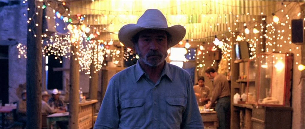 The Three Burials of Melquiades Estrada (2005) movie still: medium — An outdoor area is illuminated by strings of fairy lights at night. A…
