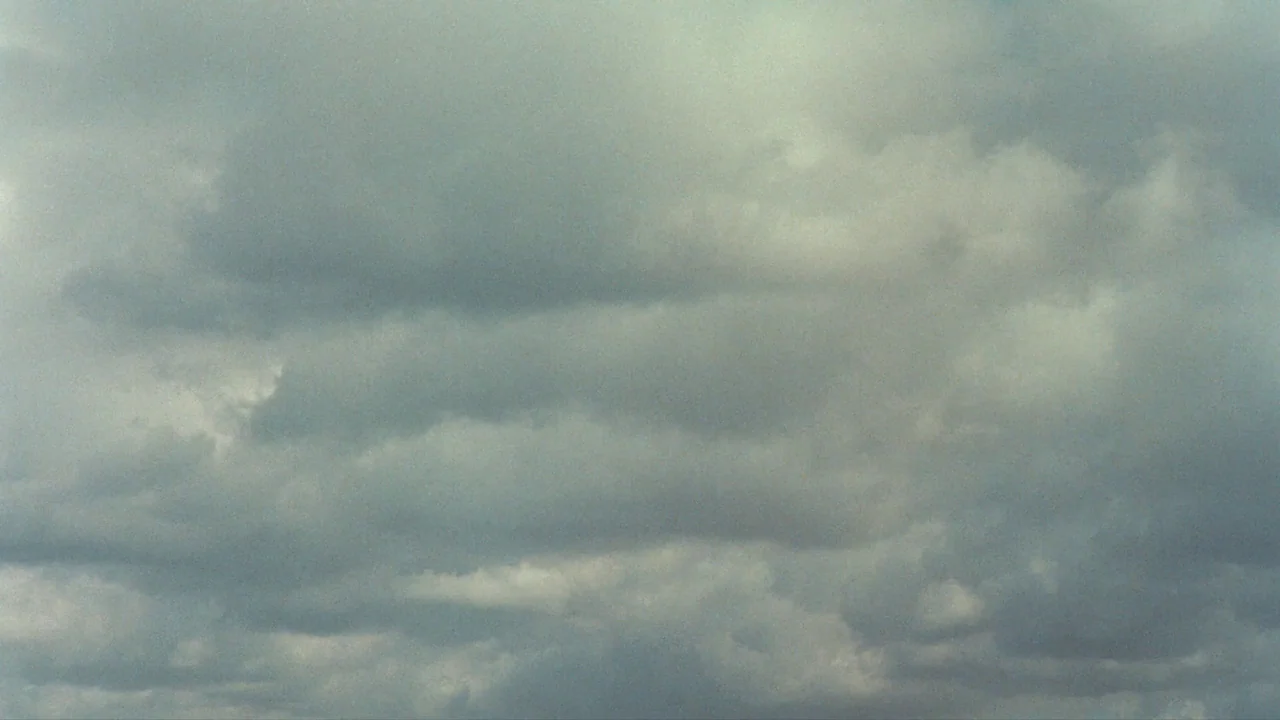 Playtime (1967) movie still: establishing — A dense layer of overcast clouds fills the entire frame. The texture is uniform across the sky with no…