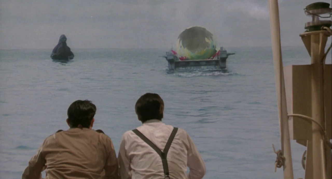 Godzilla and Mothra: The Battle for Earth (1992) movie still: wide — Two men on the deck of a boat look out at the horizon. A giant gorilla creature…